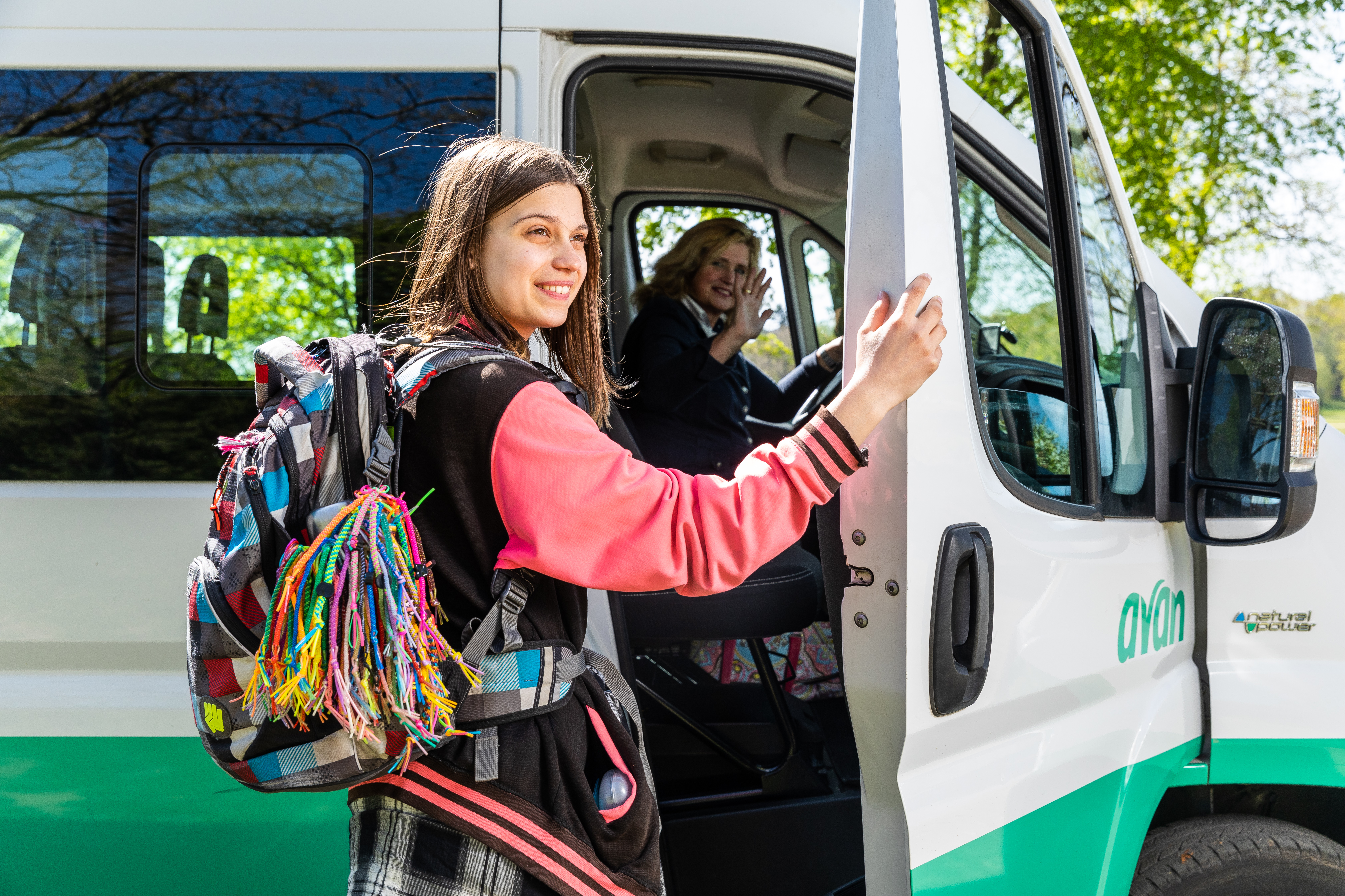 Meisje staat op het punt om de deur dicht te doen na het uitstappen, op de achtergrond zwaait de chauffeur naar haar.