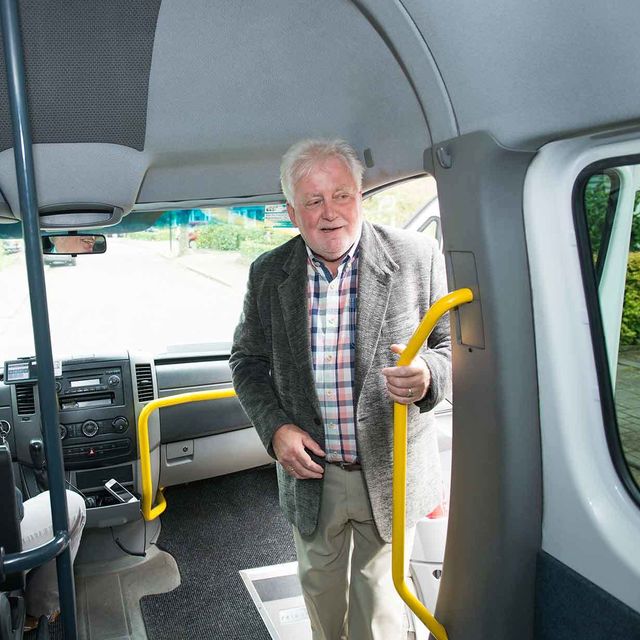 Man stapt de taxibus in terwijl hij zich vasthoudt aan de gele stang naast de deur.